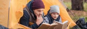 father and son reading books while lying together in tent