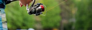 A hand holding out a fishing rod near a body of water