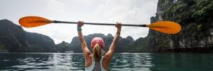 A woman holds an oar above her head while canoeing through a river