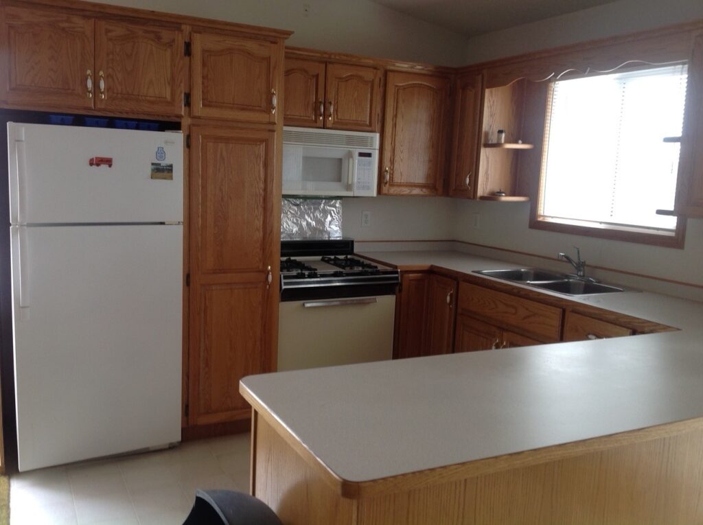 A kitchen with wooden cabinets, a white refrigerator, a microwave above a stove, and a sink under a window.