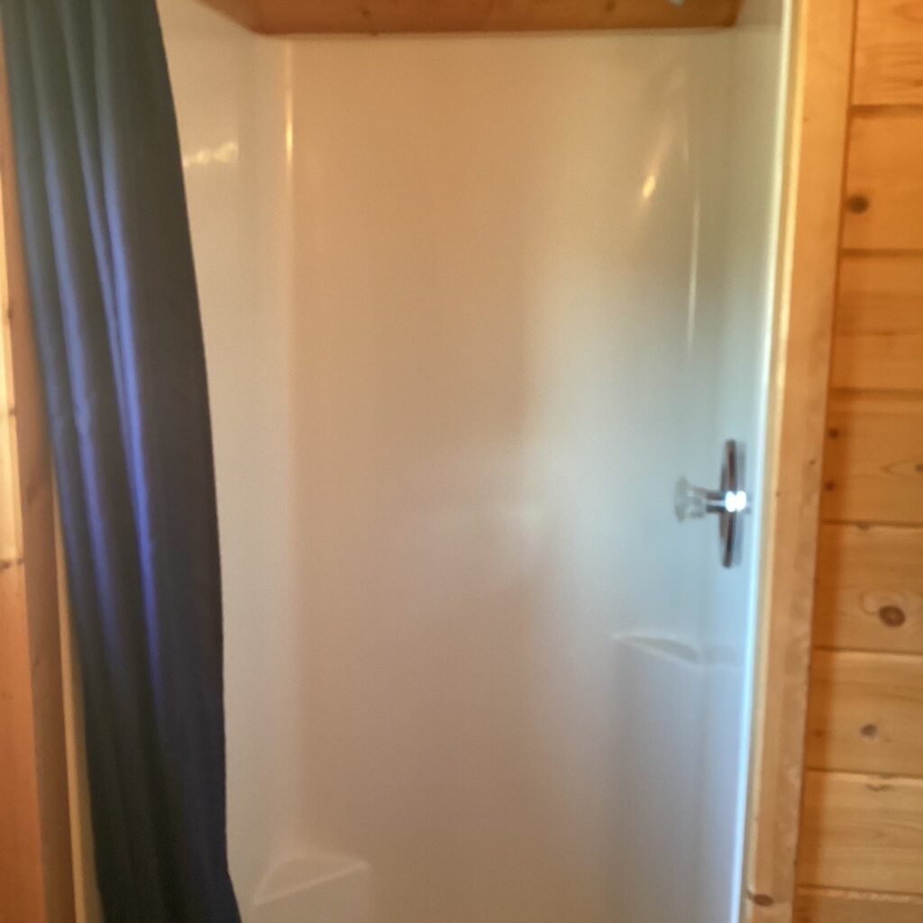 A compact, empty shower stall with a white interior and wooden walls, partially covered by a dark curtain on the left.