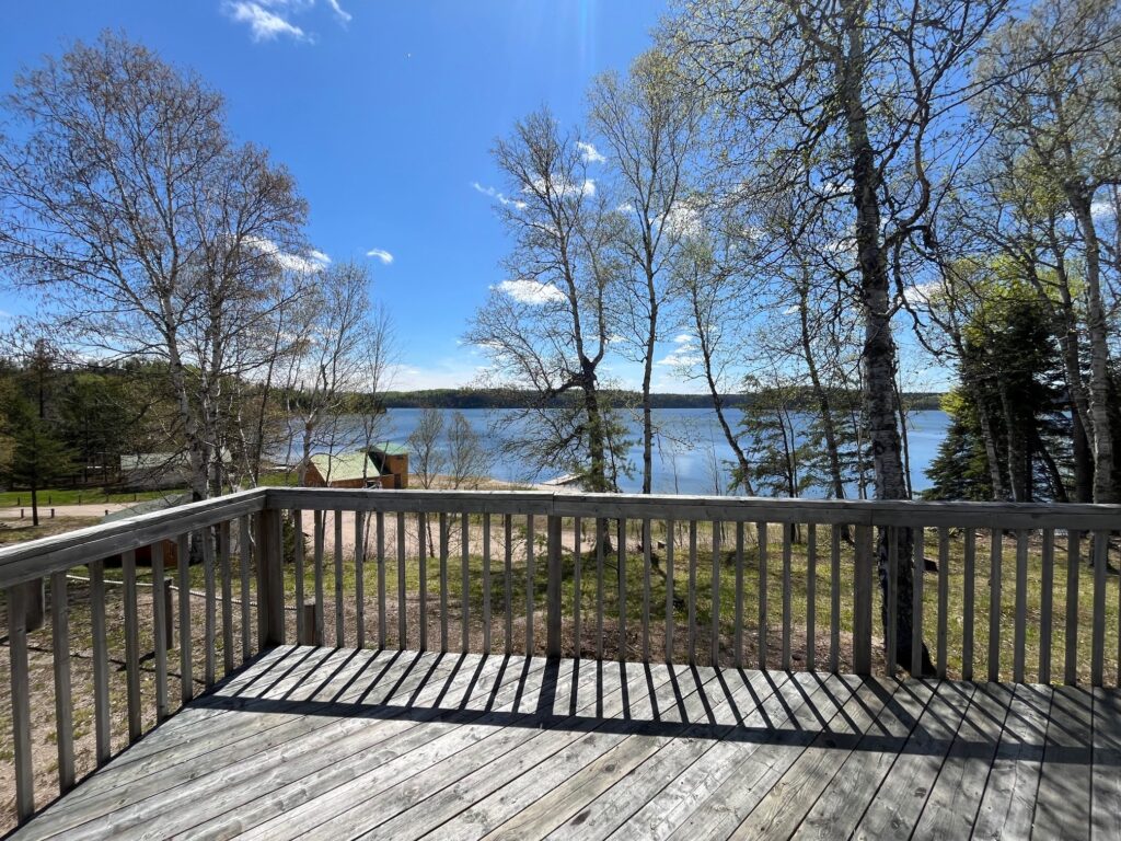 Wooden deck overlooking a lake, with trees and clear blue sky in the background.