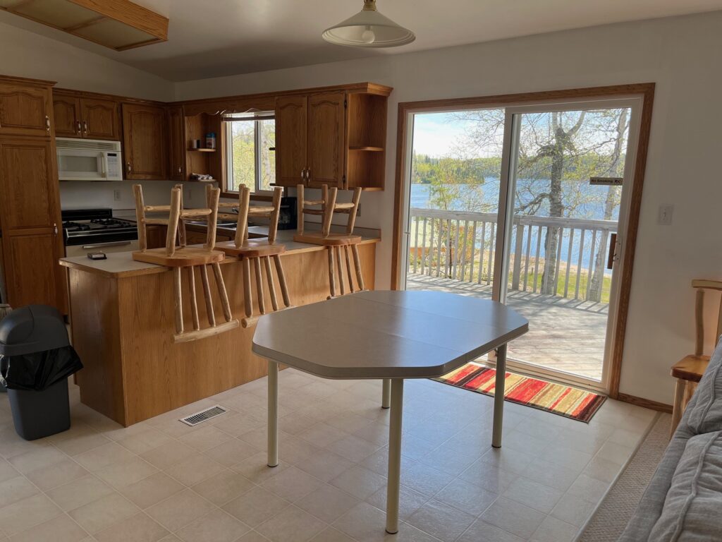 Kitchen with wooden cabinets, chairs on the island, and a folding table. Sliding door opens to a balcony with a lake view.