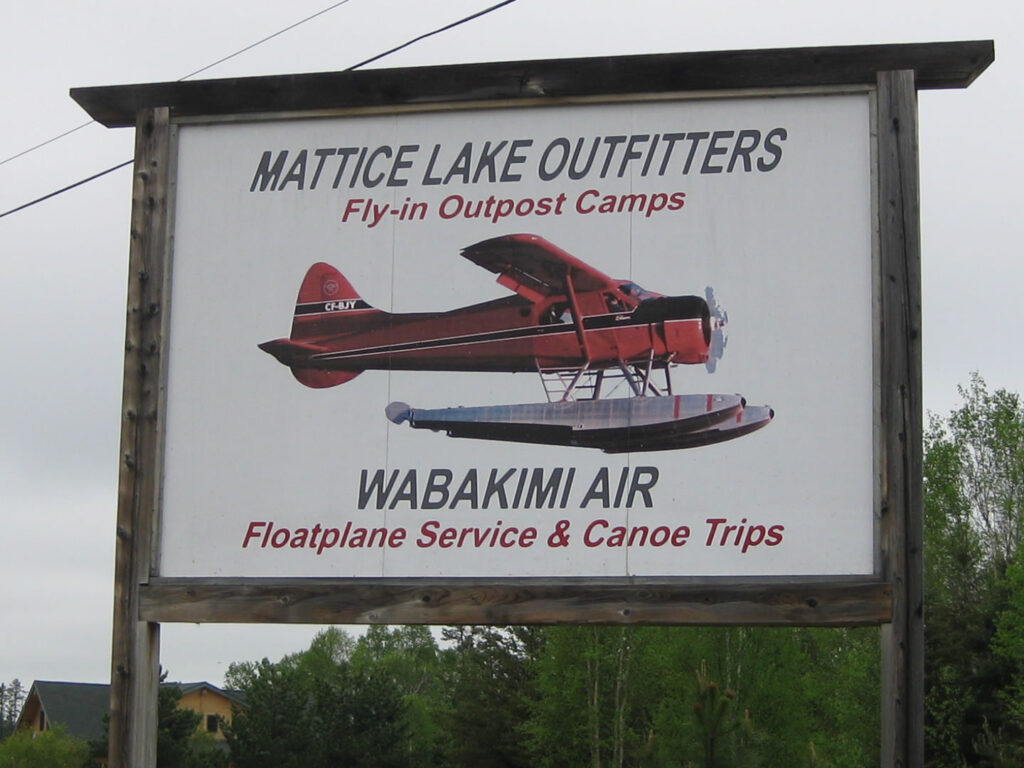 Sign for Mattice Lake Outfitters advertising fly-in camps and floatplane service, featuring an image of a red floatplane.