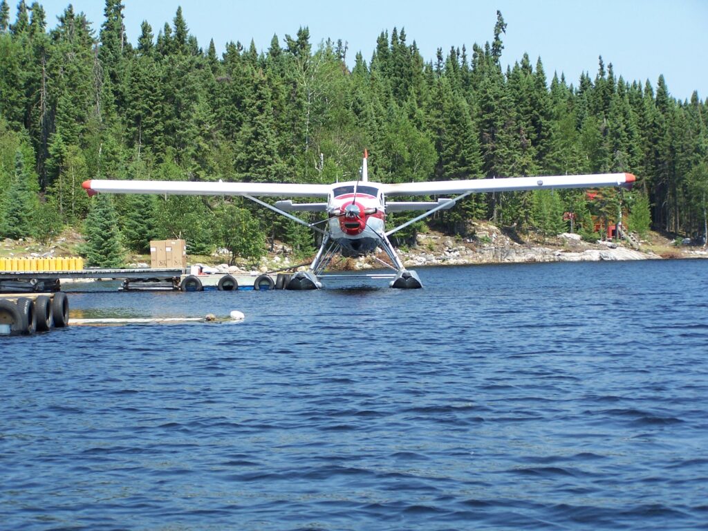 A seaplane is docked on a calm lake, surrounded by a forested shoreline under a clear sky.