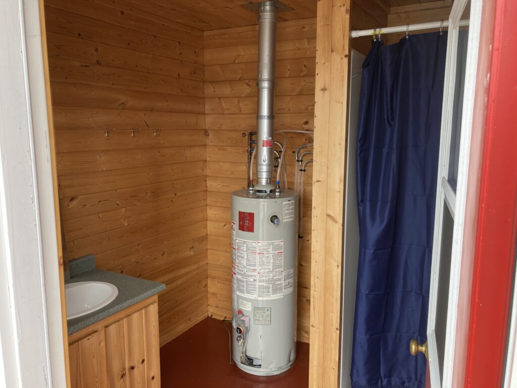 Water heater and small sink with a countertop in a wooden-walled room, beside a blue curtain.